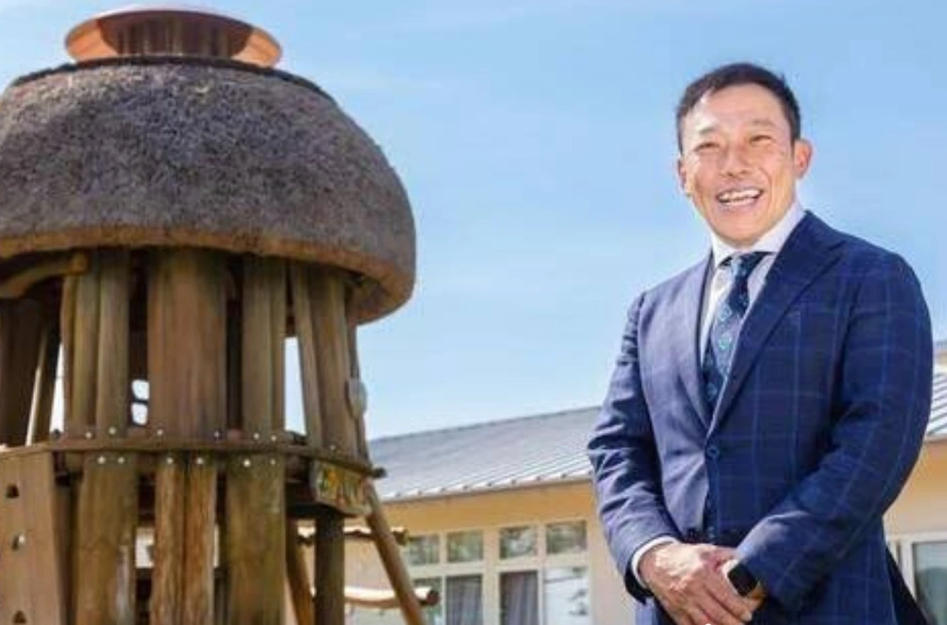 茅葺き屋根の木の塔のそばで、笑顔で立つ石井さん