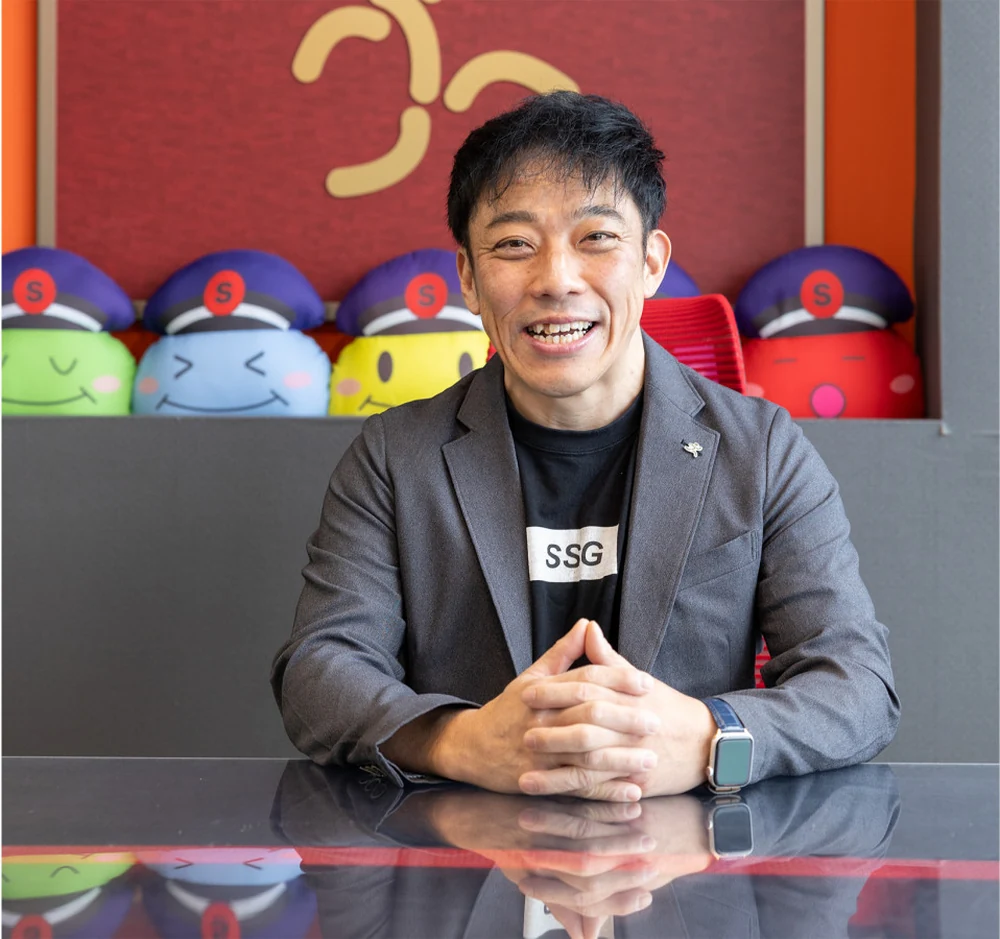 キャラクターのクッションを背に、笑顔で話す石井さん